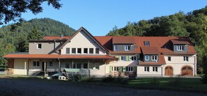 Ein großes, mehrstöckiges Gebäude mit rotem Ziegeldach, zahlreichen Fenstern und einem Eingangsbereich mit einer Veranda.