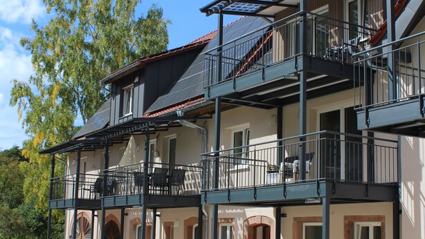 Um edifício com vários andares, varandas, um caminho de tijolos e um gramado verde.
