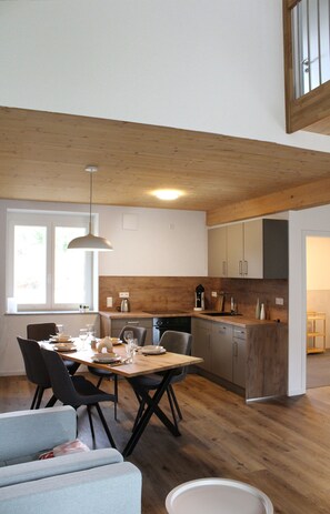 Een moderne keuken met houten kastjes, een eettafel met stoelen en een hangende lamp.