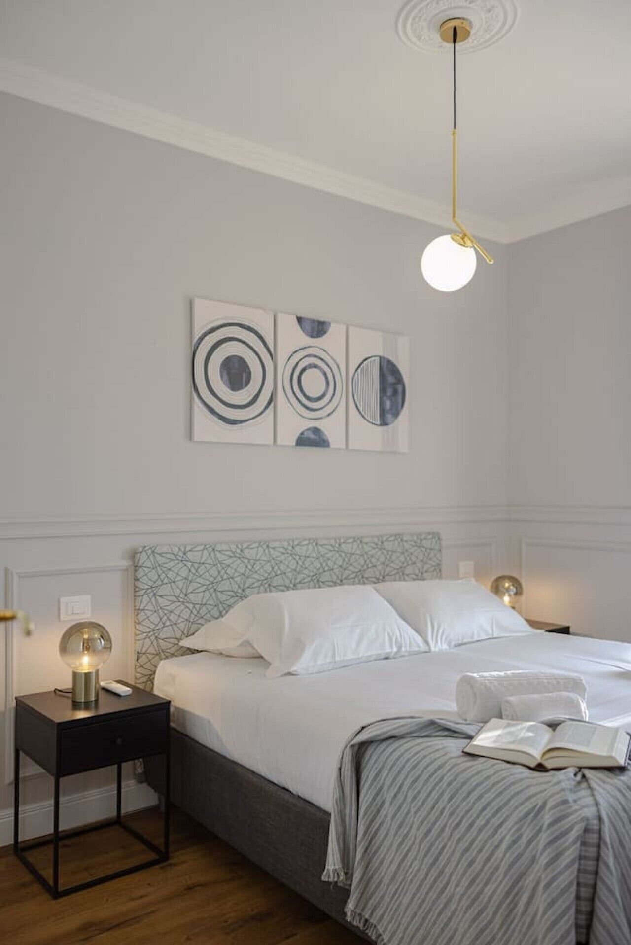 A neatly arranged bedroom with a bed, bedside tables, a lamp, and wall art.