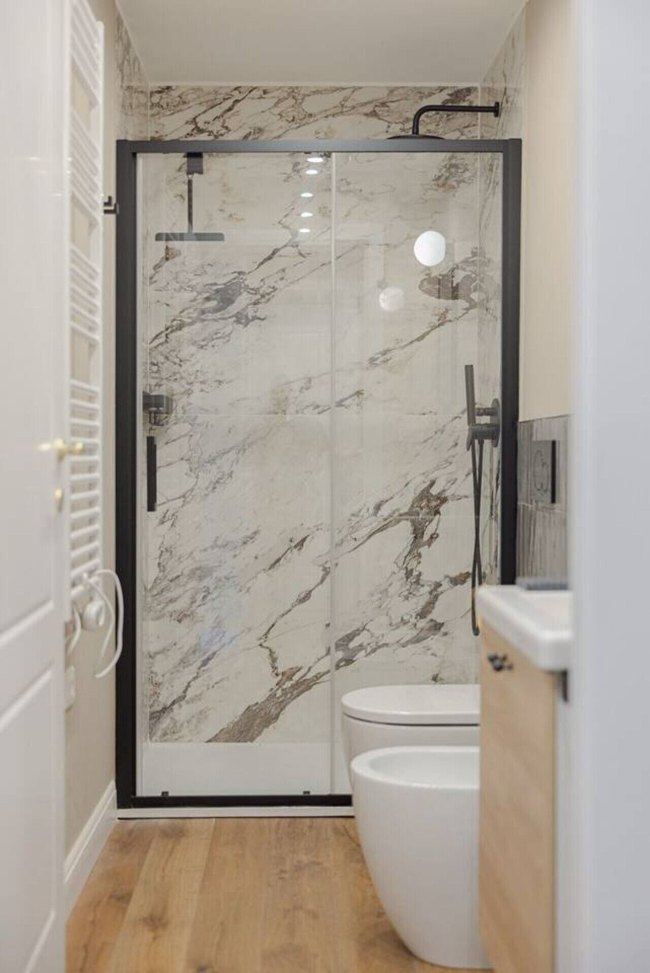 A bathroom with a glass shower enclosure, a toilet, and a wooden floor.