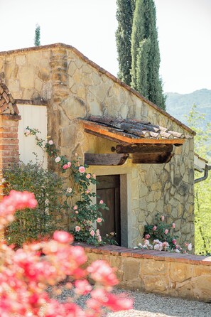 Un bâtiment en pierre avec une porte en bois, entouré d’un jardin où poussent des fleurs roses.