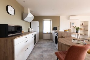 Une cuisine moderne équipée d’un four à micro-ondes, d’un four traditionnel et d’un évier, un coin repas avec une table et des chaises, et une horloge au mur.