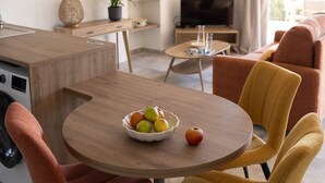 Cocina moderna con comedor, que incluye una mesa redonda con sillas, un cuenco de fruta y un televisor al fondo.
