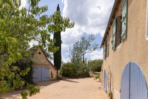 A rural property with a gravel driveway, a traditional building with a pitched roof, and a large tree in the foreground. - In the Shadow of First Names - Alice's Guesthouse (Miers)