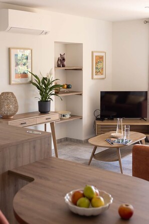 Ein modernes Wohnzimmer mit Essbereich, einem Fernseher und einer Obstschale auf dem Tisch.