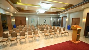 Un salón de conferencias con filas de sillas, un atril y obras de arte en las paredes.