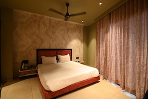 Habitación de hotel con una cama grande, un ventilador de techo, una mesita de noche y una ventana con cortinas.