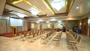A conference room with rows of chairs, a podium, a screen, and framed artwork on the walls. - Hotel Minaxi Palace (Bhinmal)