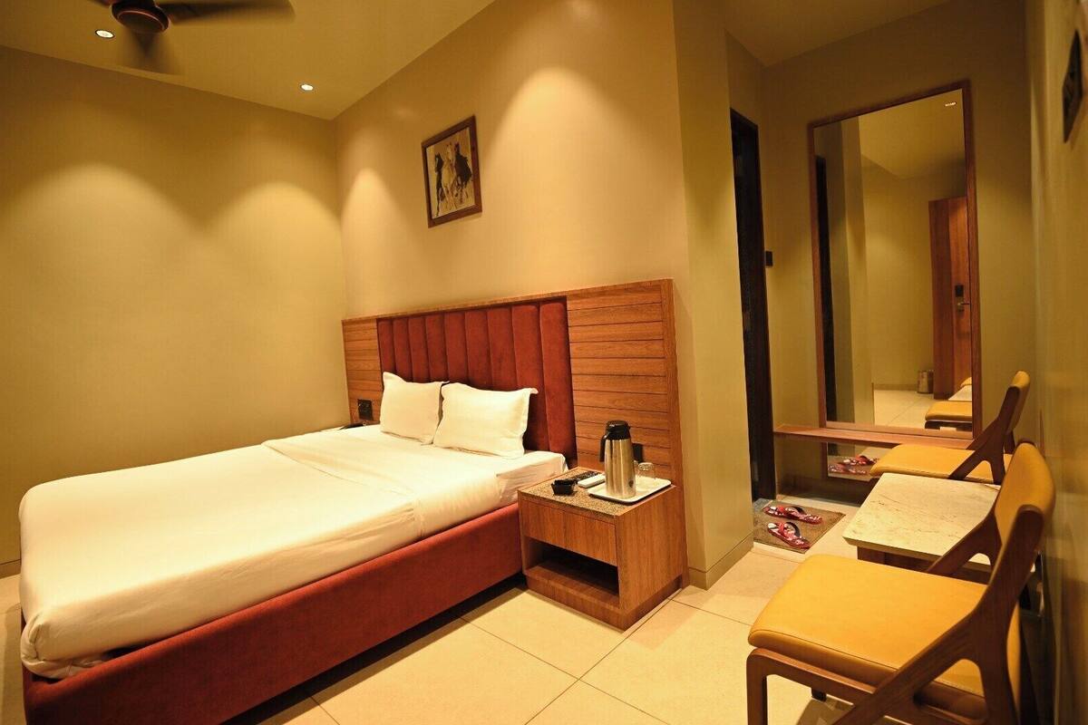 A hotel room with a bed, bedside table, chair, and a mirror.