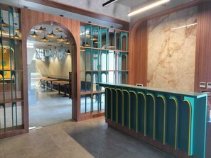 Zona de recepción con mostrador de madera, separadores de vidrio y pared de mármol.
