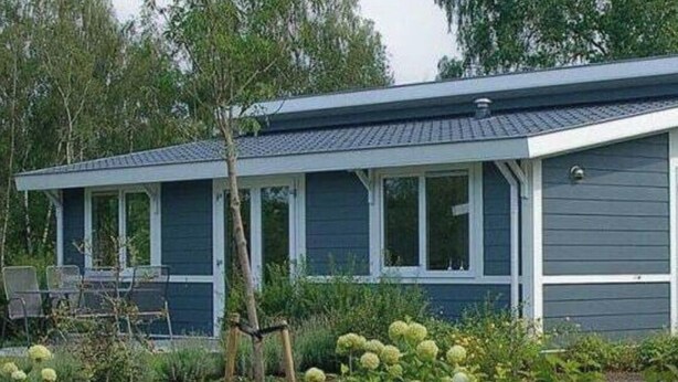 Een gelijkvloers gebouw met een overdekte veranda, omringd door een tuin met hortensia’s en een kleine boom.