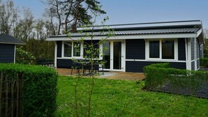 Een huis met twee verdiepingen, een overdekte patio, een omheind terras en een grote boom.