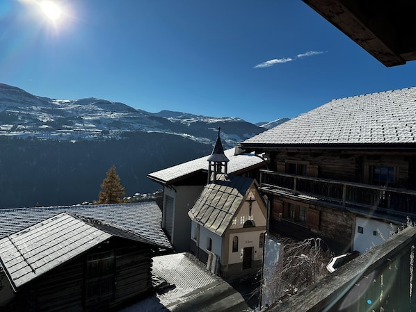 Un village de montagne aux bâtiments traditionnels en bois, une église dotée d’un clocher et une vue sur des montagnes enneigées.
