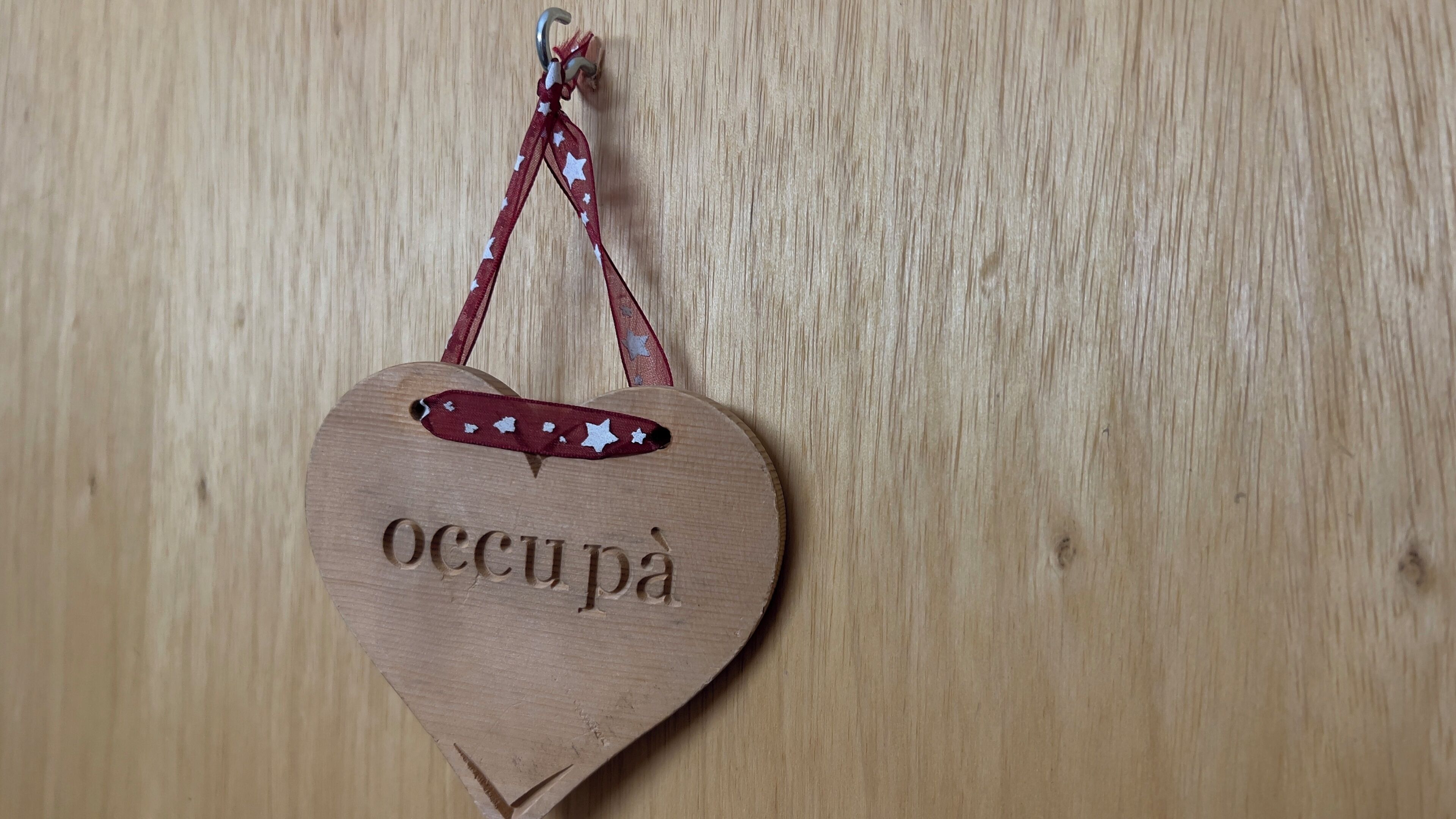 Un adorno con forma de corazón de madera con la inscripción 'occupà' y una pequeña decoración de estrella.