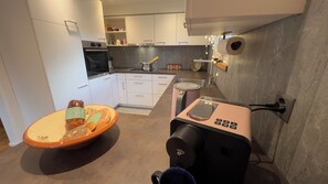 A modern kitchen with white cabinets, a built-in oven, a coffee machine, and a large orange bowl on the counter. - HYDEAWAY ANDIAST: Where nothing is a must. And everything comes into being. For your time off. (Breil-Brigels)