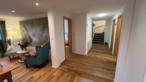 A room with a wooden floor, a patterned armchair, a small table with a vase of flowers, and a staircase leading to another level. - HYDEAWAY ANDIAST: Where nothing is a must. And everything comes into being. For your time off. (Breil-Brigels)