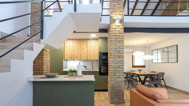 Un interior moderno con una escalera, cocina, comedor y un sofá.