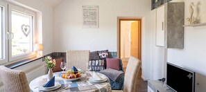 A cozy living room with a dining table set for two, a comfortable sofa, a fireplace, and a bookshelf. - Ferienwohnung Seehase (Wilhelmshaven)