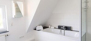 A modern bathroom with a freestanding bathtub, a glass shower enclosure, and a large mirror. - Ferienwohnung Seehase (Wilhelmshaven)