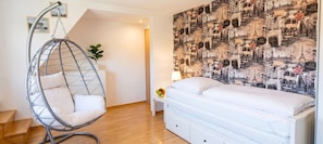 Ein Schlafzimmer mit Hängesessel, Bett, Nachttisch und einer Wand mit Stadtlandschaft-Tapete.