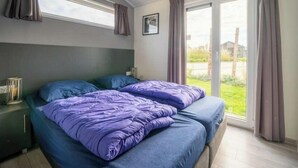 A bedroom with a bed, a nightstand, a window, and a view of the outdoors. - Hackfort Waterfront 6 (Linden)