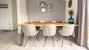 A modern dining room with a wooden table, four chairs, and a vase with flowers. - Hackfort Waterfront 6 (Linden)