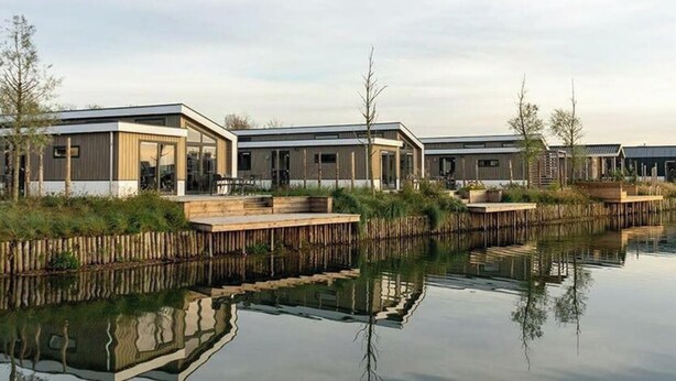 A row of modern, single-story cabins with large windows, situated next to a calm body of water. - Hackfort Waterfront 6 (Linden)