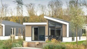 A modern house with a deck by a body of water, large windows, and a dining area. - Hackfort Waterfront 6 (Linden)