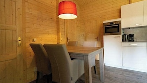 A wooden interior with a dining table and chairs, a kitchen area with appliances, and a red hanging light fixture. - Holiday Home in Maarn With Terrace (Maarn)