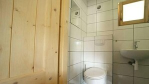 A bathroom with white tiled walls, a white toilet, a wooden door, and a small window. - Holiday Home in Maarn With Terrace (Maarn)