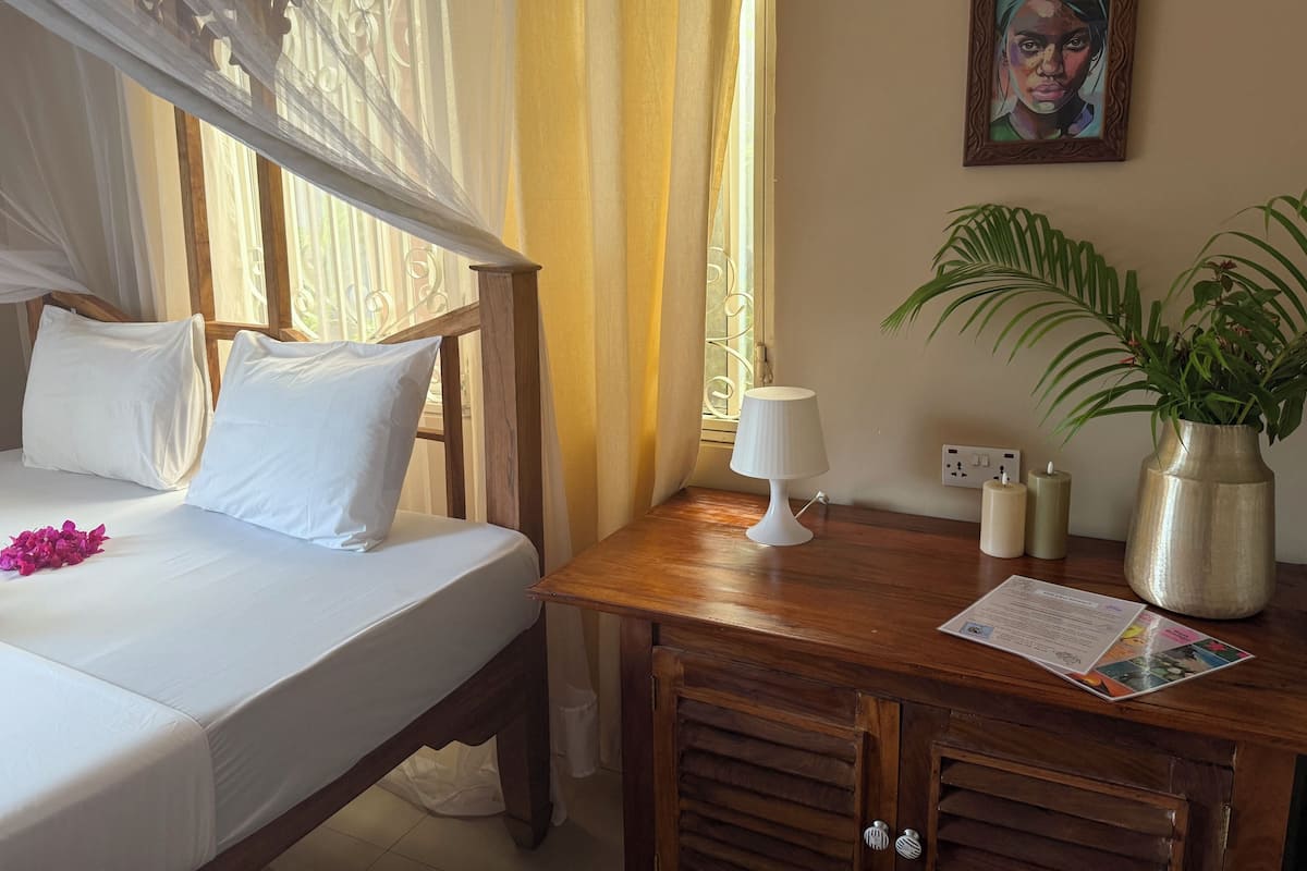 Een hotelkamer met een bed, een nachtkastje met een lamp, een vaas met planten en een schilderij aan de muur.