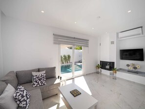Ein modernes Wohnzimmer mit grauem Sofa, Flachbildfernseher und Blick auf einen Pool.