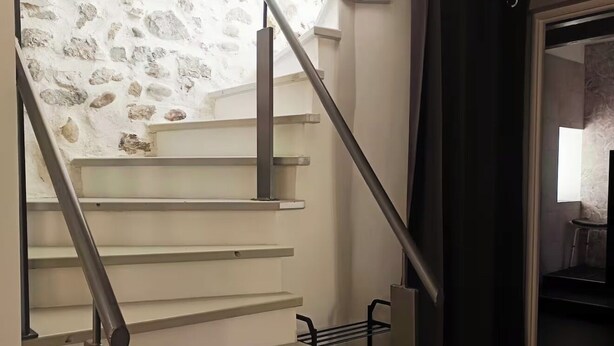 A staircase with a stone wall, metal handrails, and a dark curtain.