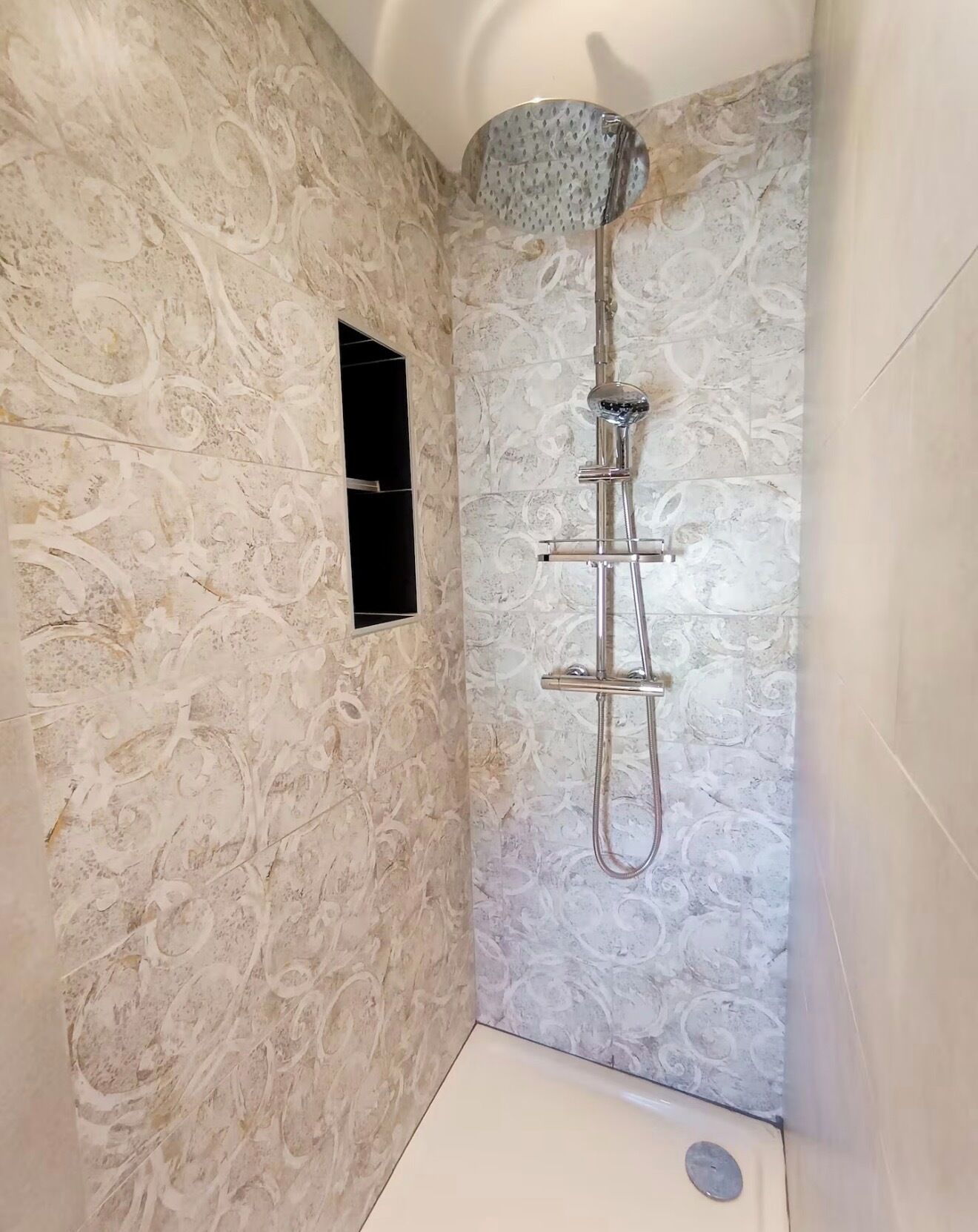 A shower with a handheld showerhead, a wall-mounted control panel, and a small window.