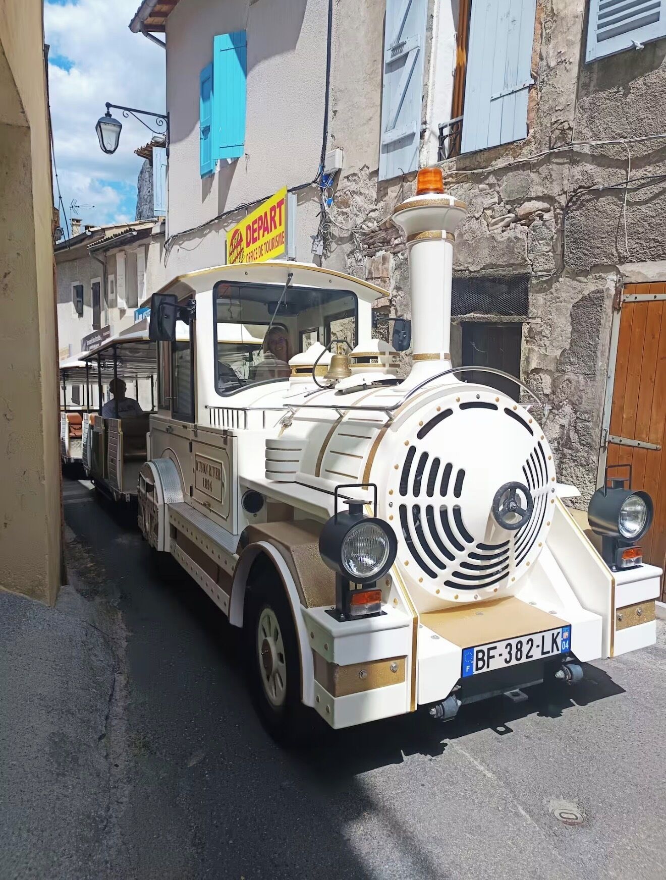 A vintage white bus with a license plate, parked on a narrow street.