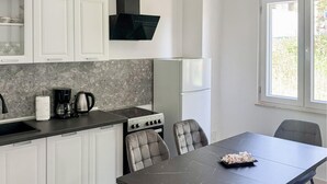 Moderni keittiö, jossa on valkoiset kaapit, musta työtaso, liesi ja ruokapöytä tuoleineen.