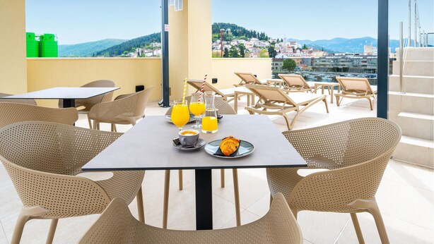 A rooftop terrace with outdoor seating, a table with breakfast items, and a scenic view of a city and hills.