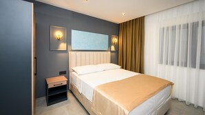 A hotel room with a bed, bedside table, wall-mounted light, and a window with curtains.