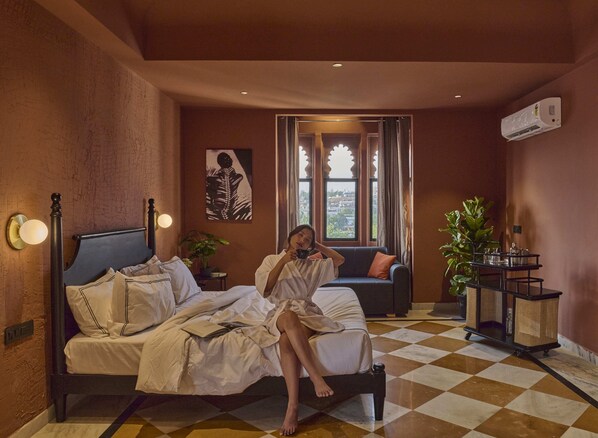 A room with a bed, a sofa, a window with curtains, a plant, and a wall-mounted air conditioner. - Minimalist - Lake Pichola Edit (Udaipur)