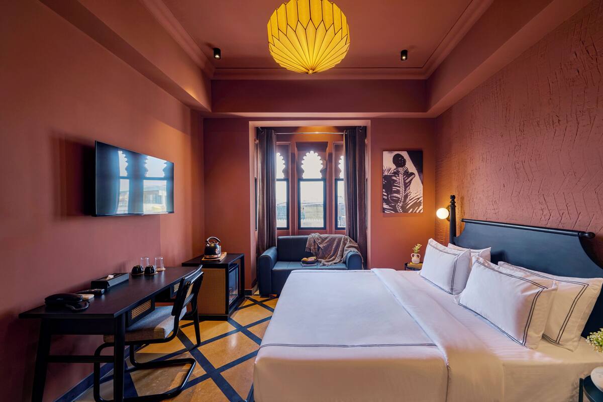 Ein Hotelzimmer mit Bett, Schreibtisch, Stuhl, Fernseher und einem großen Fenster.