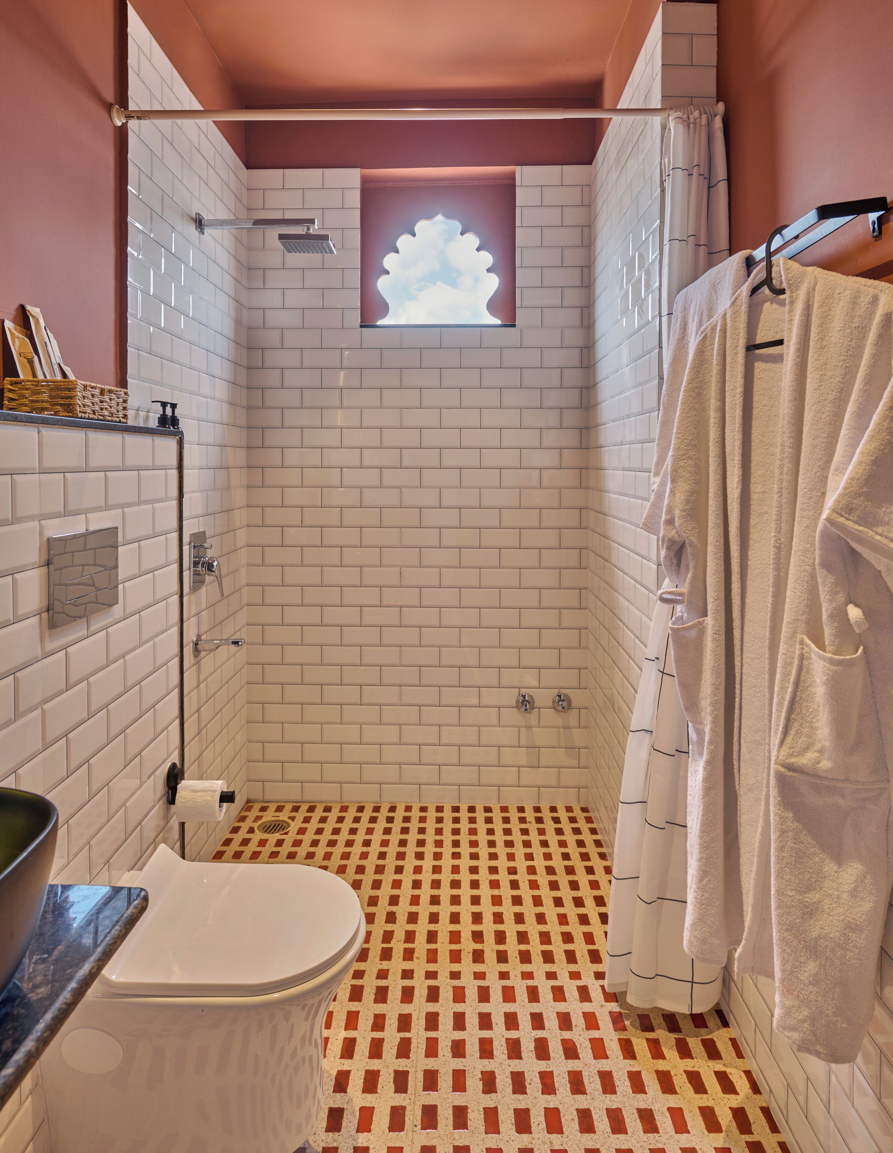 A bathroom with a shower, toilet, and a window with a cloud design.