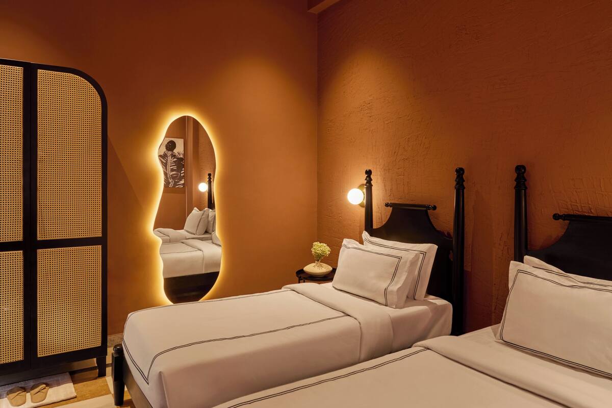 Ein Hotelzimmer mit zwei Betten, einem Spiegel, einem Nachttisch und einer dekorativen Leuchte.