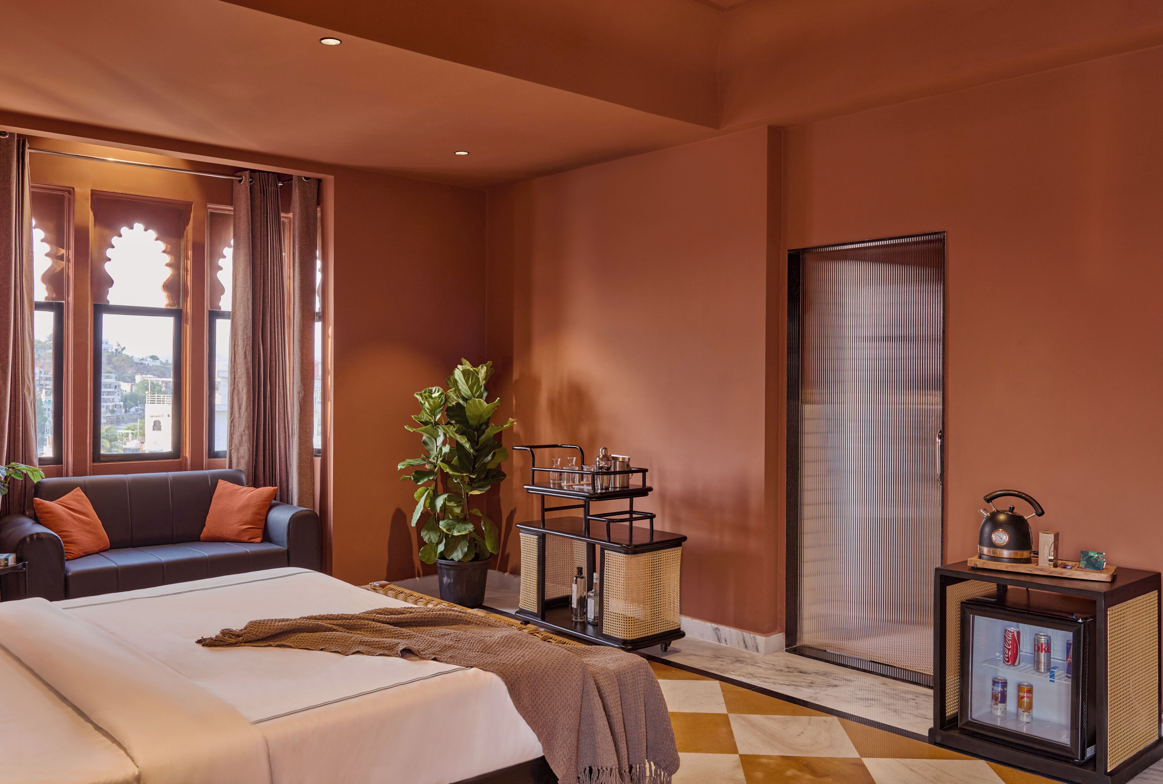 A hotel room with a bed, a sofa, a plant, a tray table with drinks, and a minibar.
