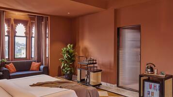 A hotel room with a bed, a sofa, a plant, a tray table with drinks, and a minibar.
