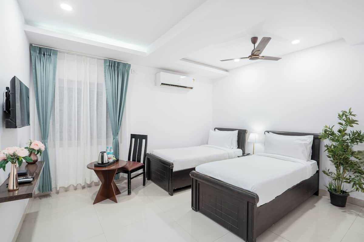A hotel room with two beds, a desk, a chair, a TV, an air conditioner, and a ceiling fan.