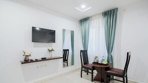 A hotel room with a flat-screen TV mounted on the wall, a small table with chairs, a vase with flowers, and a window with curtains. - RCC Hotels Park View Inn Miyapur (Hyderabad)