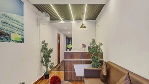 A reception area with a wooden reception desk, a brown sofa, potted plants, a round table with a red flower centerpiece, and a painting on the wall. - RCC Hotels Park View Inn Miyapur (Hyderabad)