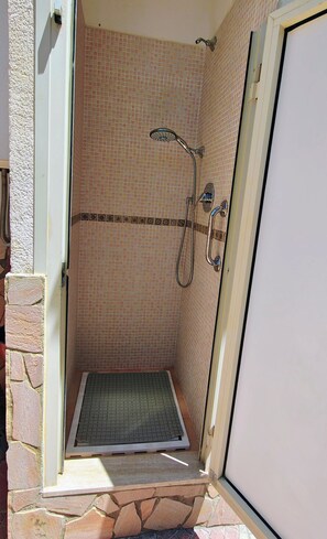 Une douche avec un mur carrelé, un pommeau de douche et un drain.