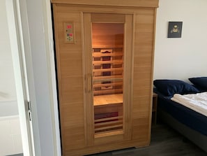 Ein Holzschrank mit Bedienfeld, ein Bett mit dunkelblauer Bettwäsche und ein kleines Bild an der Wand.